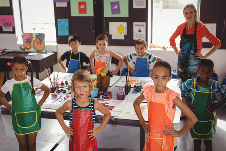 Portrait of teacher and schoolkids standing with hands on hip in drawing classの写真素材