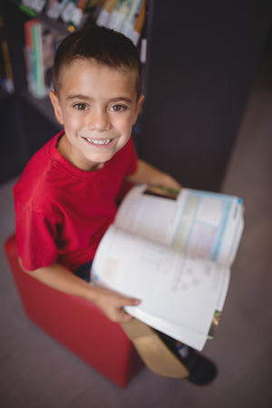 Portrait smiling schoolboy reading book in library at schoolの写真素材