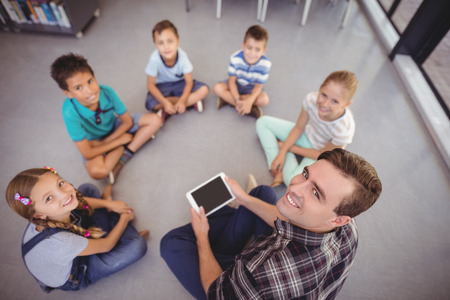 Overhead view of teacher and schoolkids using digital tablet in library at schoolの写真素材