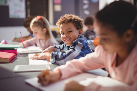 Portrait of smiling schoolboy doing his homework in classroom at schoolの写真素材