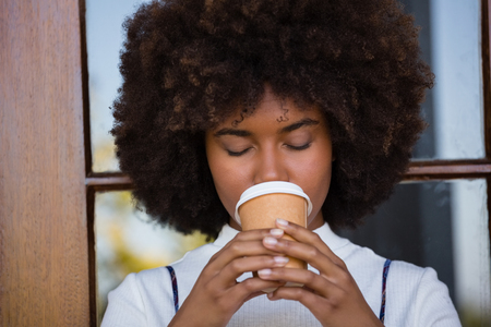Close up of woman with frizzy hair drinking coffee against doorの写真素材
