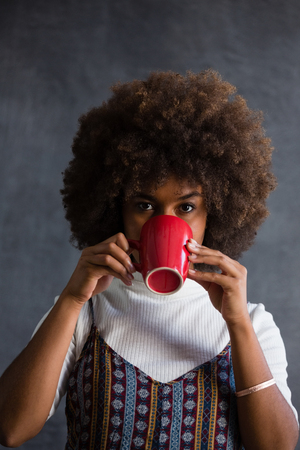 Portrait of woman with frizzy hair drinking coffee against wallの写真素材