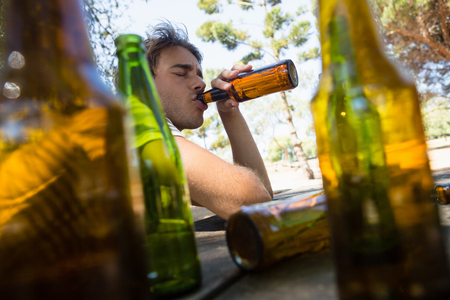 Unconscious man drinking beer from bottle in the parkの写真素材