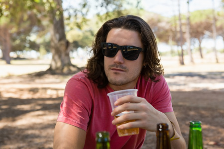 Young man in sunglasses having beer in the park