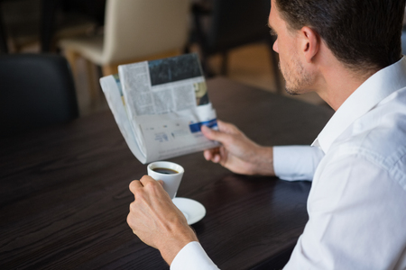 Businessman reading newspaper while having coffee at table in cafeの写真素材