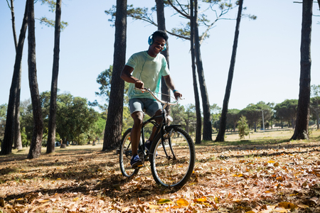 Young man with headphones riding bicycle in the parkの写真素材