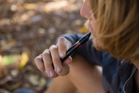Thoughtful man smoking an electronic cigarette in the parkの写真素材