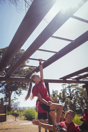Trainer assisting kids to climb monkey bars during obstacle course training at boot camp