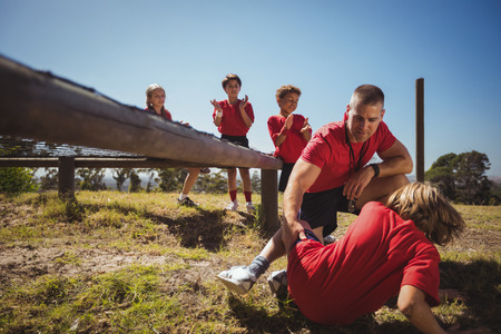 Trainer assisting kids in the obstacle course training on a sunny day