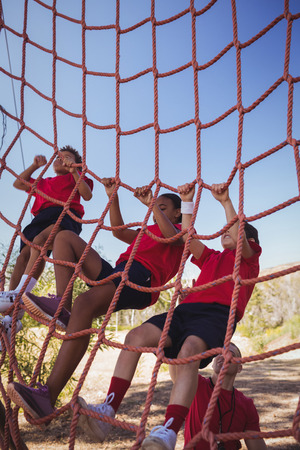 Trainer assisting boy to climb a net during obstacle course training in the boot campの写真素材