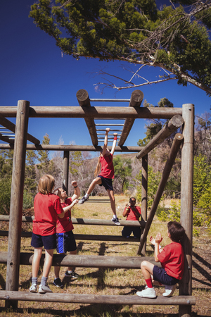 Trainer assisting girl to climb monkey bars during obstacle course training in the boot camp