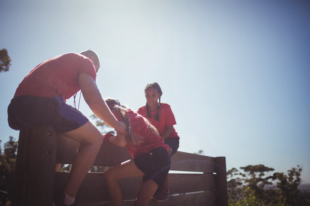 Trainer assisting kids to climb a wooden wall during obstacle course training at boot campの写真素材