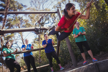 Fit woman climbing a rope during obstacle course training in the boot camp