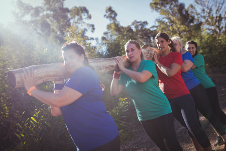 Group of fit women carrying a heavy wooden log during obstacle course training in the boot campの写真素材