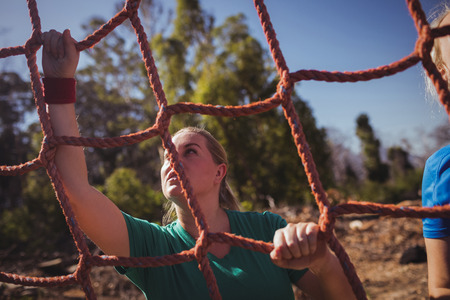 Fit woman climbing a net during obstacle course training in the boot campの写真素材