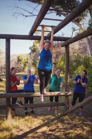 Woman being cheered bye her teammates to climb monkey bars during obstacle course training in the boot campの写真素材
