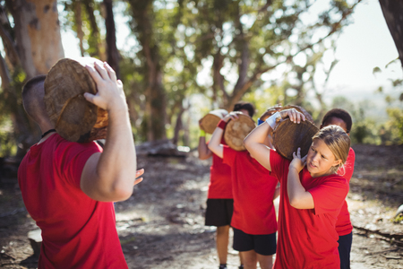 Trainer and kids carrying wooden logs during obstacle course training in the boot camp