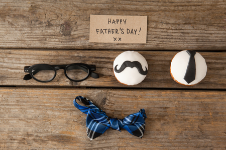Overhead view of happy fathers day text on paper by decorated cupcakes and eyeglasses at wooden tableの写真素材