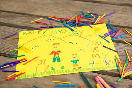 Close up of fathers day greeting card with crayons on wooden table
