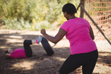 Trainer assisting woman while exercising during obstacle course in boot campの写真素材