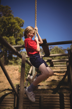 Portrait of smiling girl climbing rope during obstacle course in boot campの写真素材