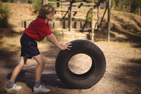 Determined girl exercising with huge tyre during obstacle course in boot campbootの写真素材