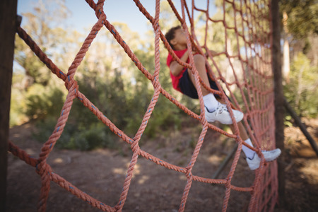 Determined boy climbing a net during obstacle course in boot campの写真素材
