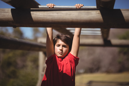Portrait of boy exercising on monkey bar during obstacle course in boot camp