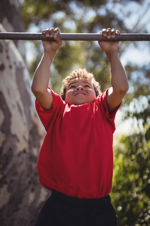 Boy performing pull-ups on bar during obstacle course in boot campの写真素材