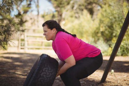 Determined woman exercising with huge tyre during obstacle course in boot campの写真素材