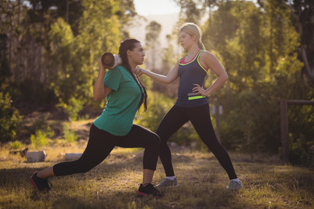 Trainer assisting woman in exercising during obstacle courseの写真素材