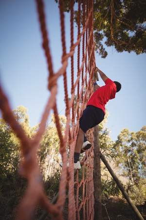 Boy climbing a net during obstacle course in campの写真素材