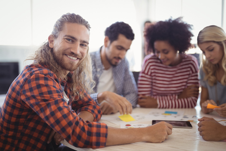 Portrait of smiling young businessman sitting with colleagues at office deskの写真素材