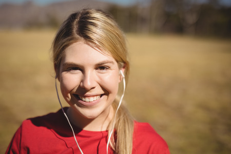 Portrait of fit woman listening music on headphones during obstacle course in boot campの写真素材