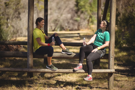Happy friends relaxing on obstacle during obstacle course in boot campの写真素材