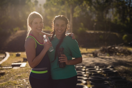 Portrait of happy friends holding water bottle during obstacle course in boot campの写真素材