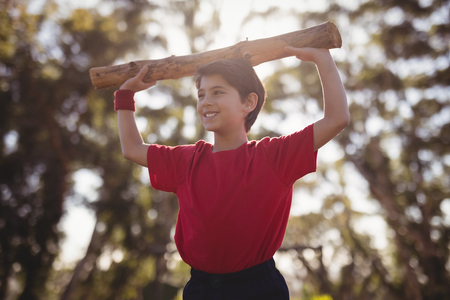 Happy boy exercising with log during obstacle course in boot campの写真素材