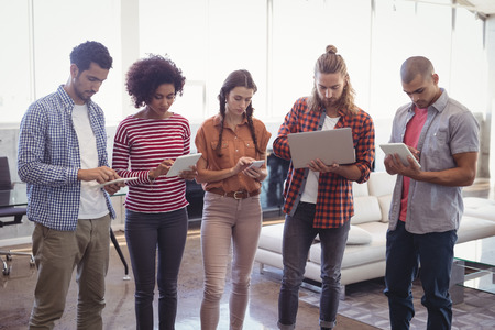 Young creative business people using laptop and digital tablets while standing at office