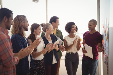 Smiling young businessman explaining to creative team standing at office