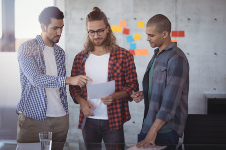 Creative business team discussing over paper while standing in officeの写真素材