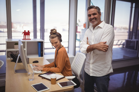 Portrait of happy businessman standing while female colleague working in officeの写真素材