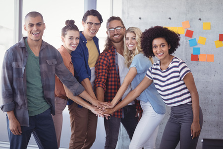 Portrait of cheerful business team stacking hands in creative officeの写真素材