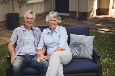 Portrait of happy senior couple sitting on couch in backyard