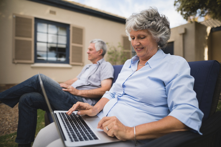 Senior woman using laptop while sitting on couch with man in backyardの写真素材