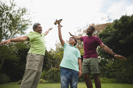 Low angle view of boy holding toy airplane with father and son at parkの写真素材