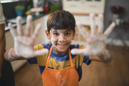 Portrait of smiling boy showing messy palms while standing in kitchenの写真素材