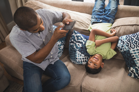 High angle view of man photographing his son lying on couch at homeの写真素材