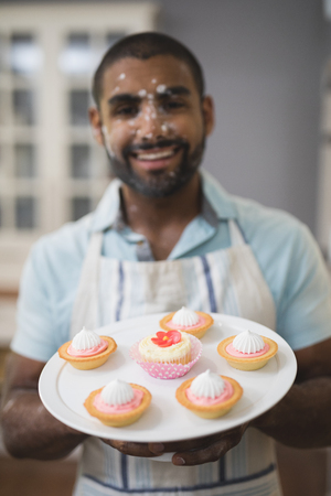 Portrait of happy man with desserts on plate in kitchenの写真素材