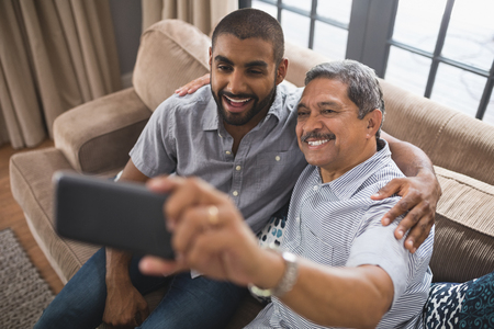 Happy man with his son taking selfie while sitting together on couch at home