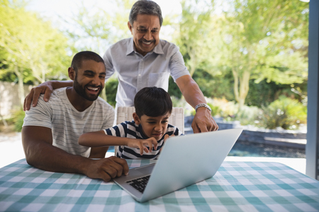 Cheerful multi-generation family using laptop together on table at porch